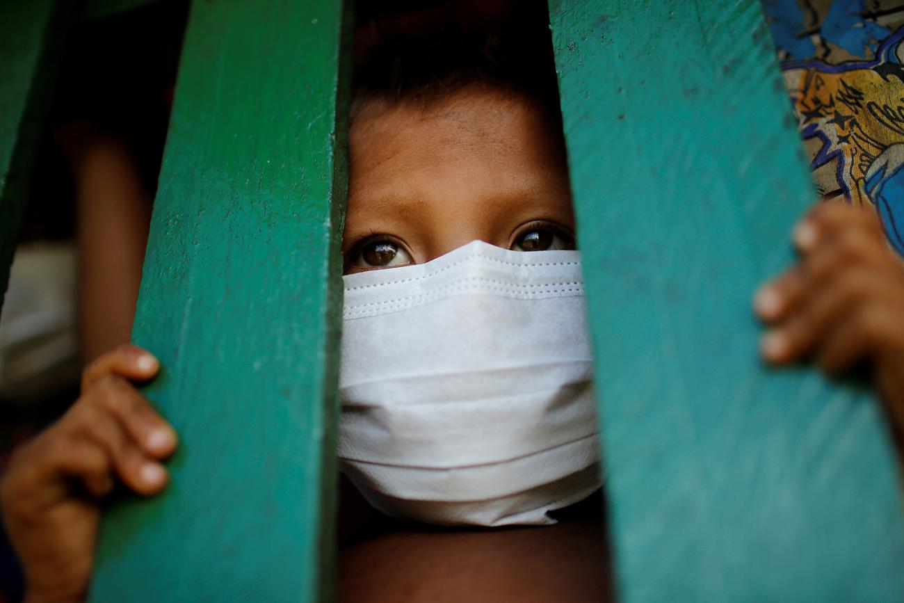 The photo shows a boy wearing a mask peeking through green slats.