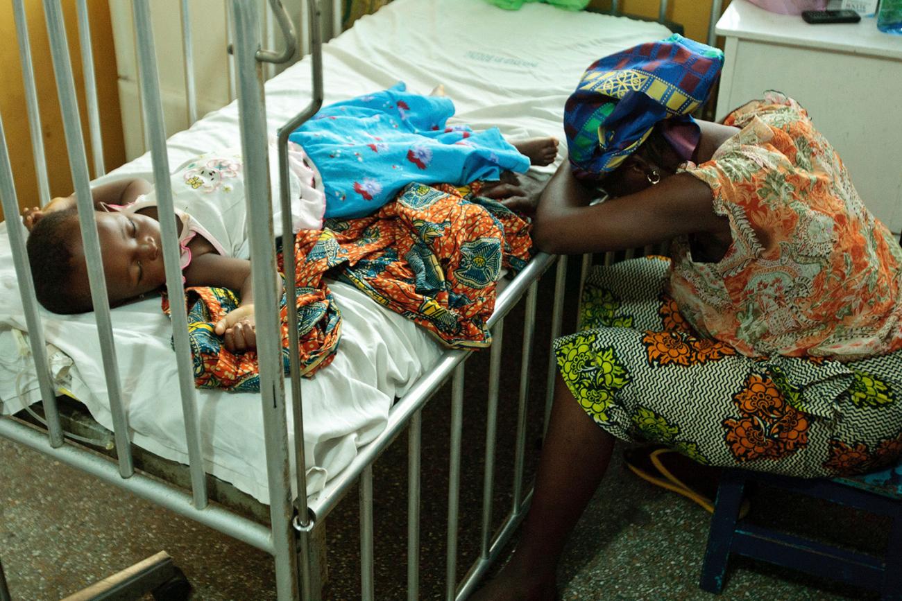 Picture shows the mother with her head buried in her arms leaning over her daughter's sick bed.