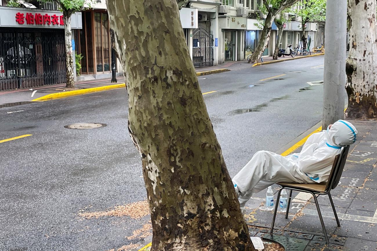 A man in a protective suit slumps as he rests on a bench on an empty street during a COVID-19 outbreak in Shanghai, China, on April 23, 2022.