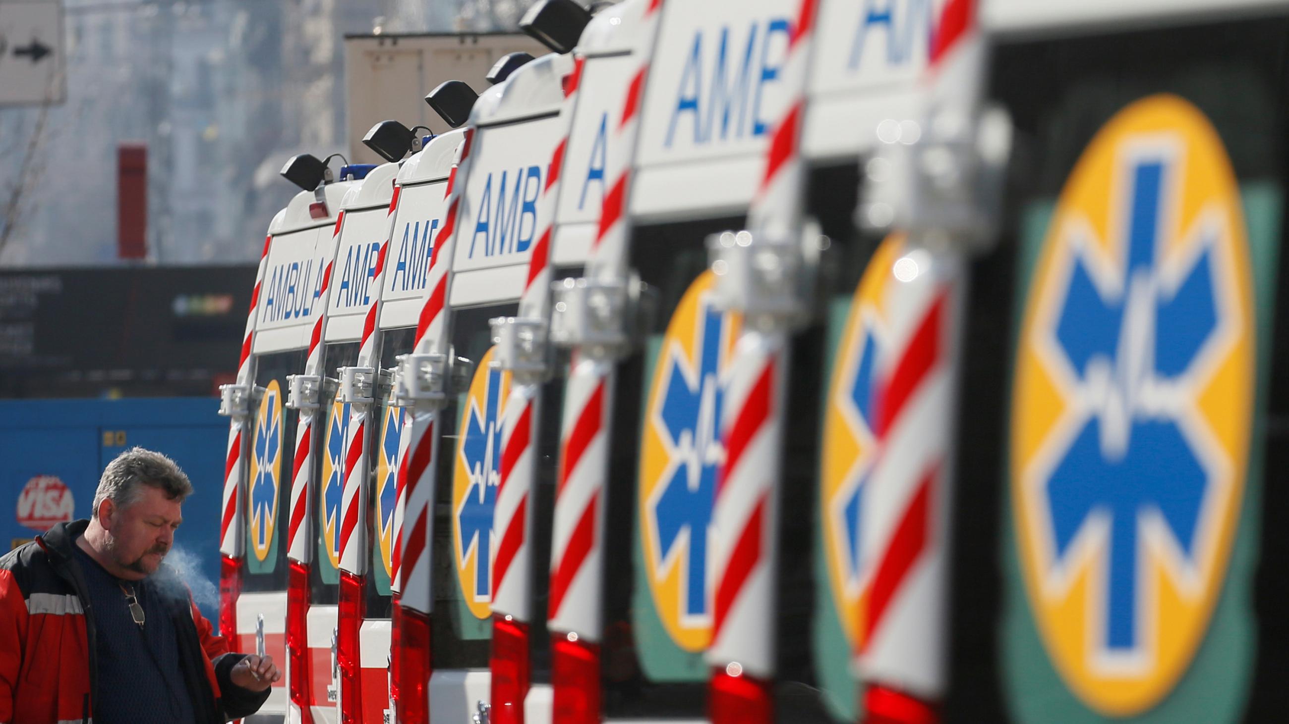 The photo shows a long line of ambulances with a worker at the end puffing on a cigarette.