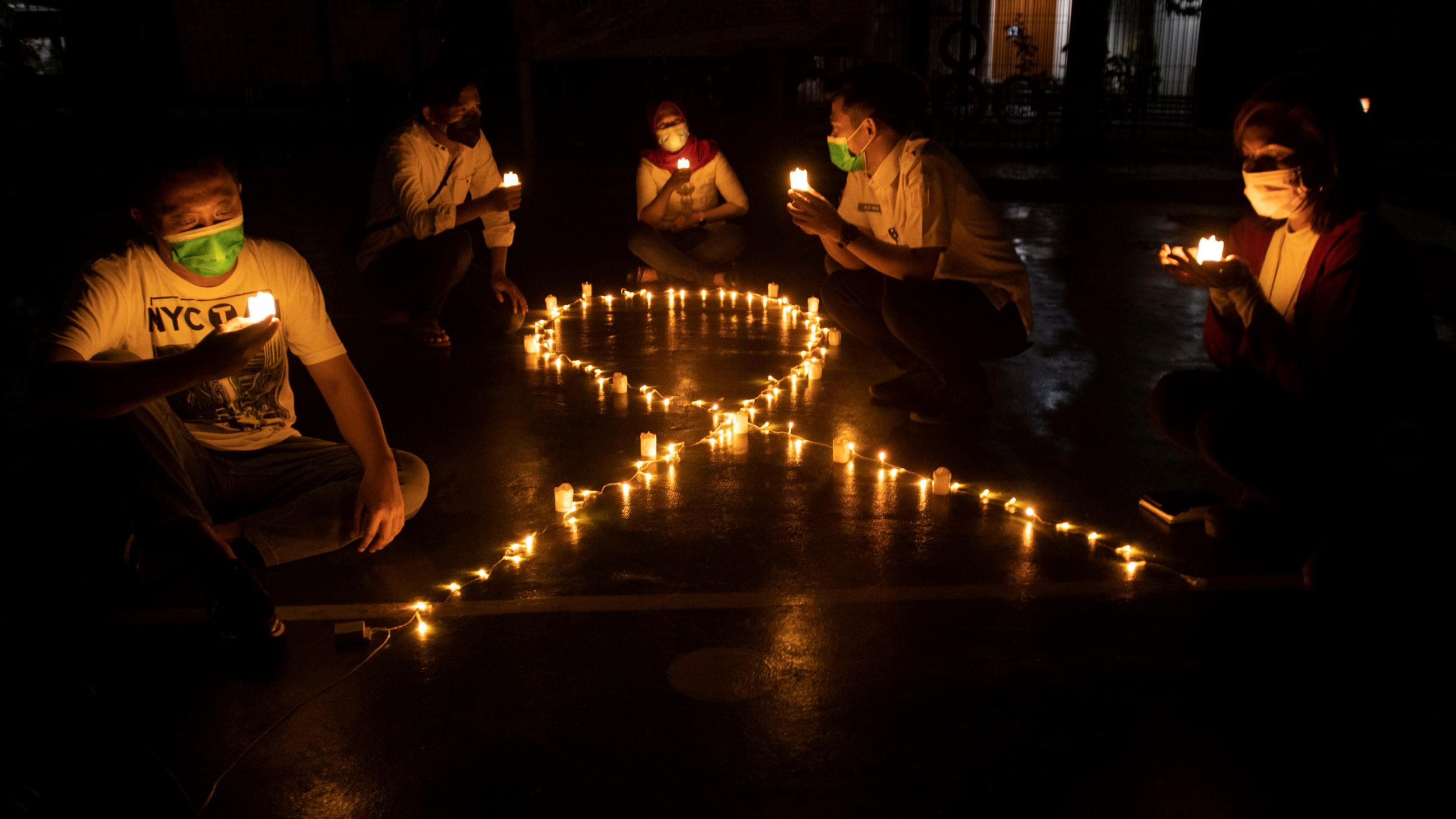 Activists sit next to candles laid out in the shape of an AIDS ribbon, commemorating World Aids Day in Jakarta, Indonesia, on December 1, 2021.Â